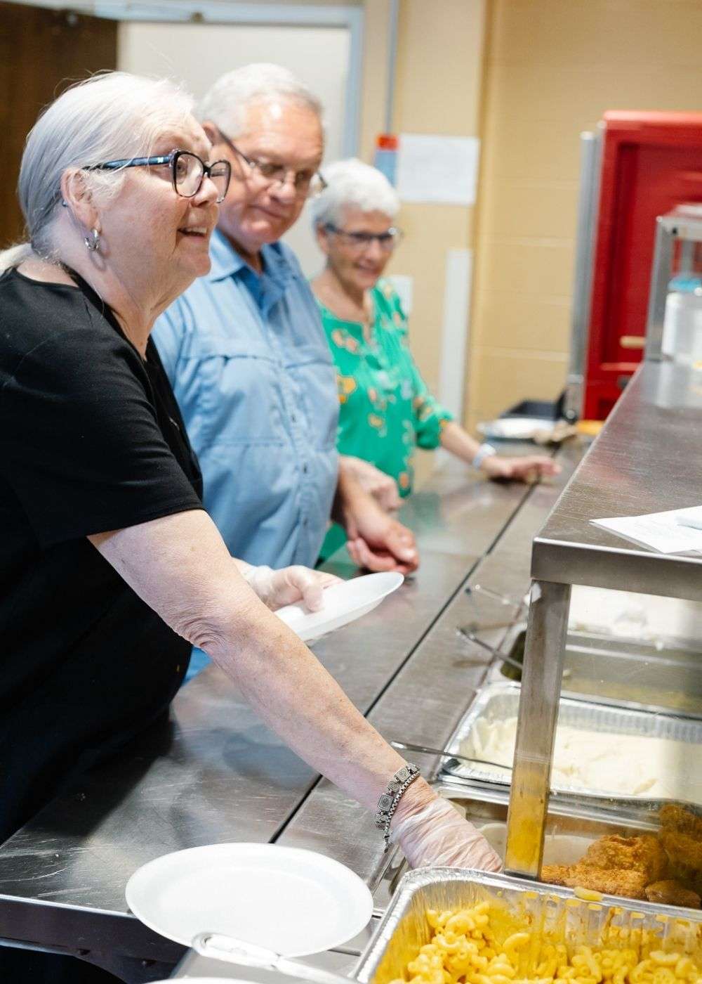 3 adults serving food on a food line in the kitchen at LaGrange First united Methodist Church Soup Kitchen